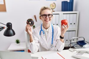 uśmiechnięty lekarz trzyma pączka i jabłko